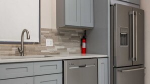 A kitchen with grey cabinets, a stainless steel refrigerator, a built-in oven, and a water dispenser.