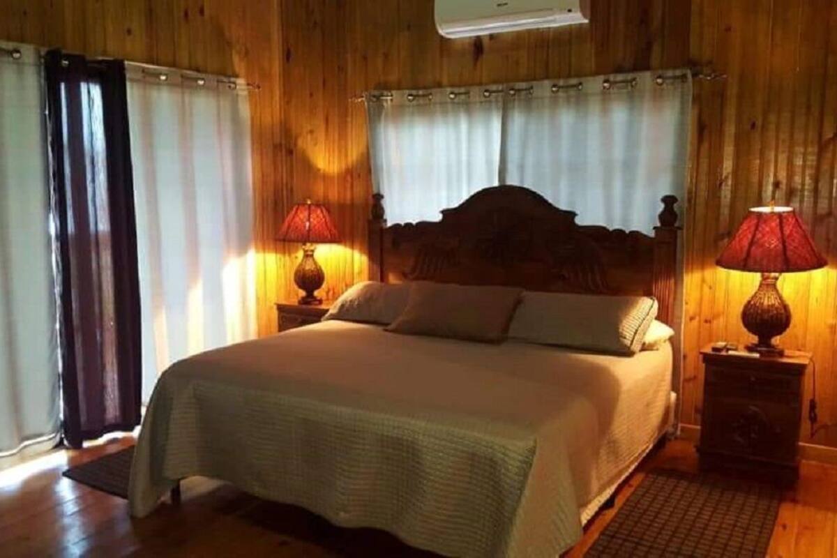 Quarto com painéis de madeira, uma cama, duas luminárias de cabeceira e uma janela com cortinas.