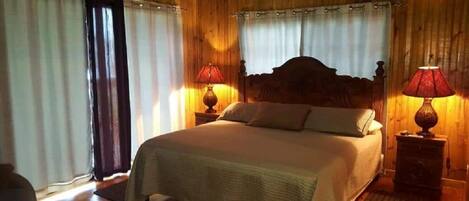 Un dormitorio con paneles de madera, una cama, dos lámparas de noche y un ventanal con cortinas.