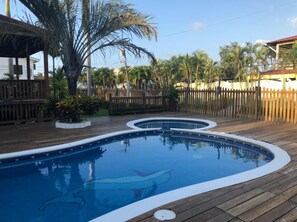 A swimming pool with a wooden deck, surrounded by a wooden fence and palm trees.