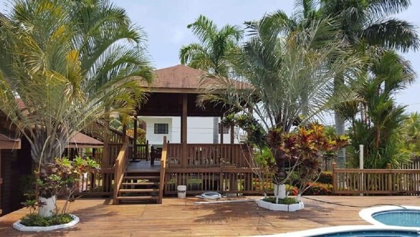 Una terraza de madera con piscina, rodeada de palmeras y un edificio con balcón.