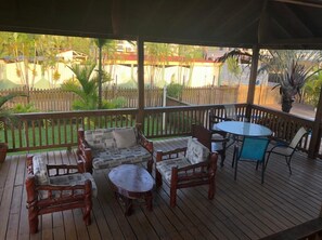 A covered outdoor patio with wooden furniture, including sofas and a table, surrounded by a wooden fence.