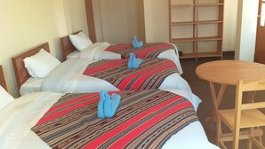 Habitación de hotel con dos camas, cada una con una manta a rayas y pantuflas azules. Hay una silla de madera y una mesita redonda.