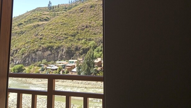 Vista a través de una ventana de un río, edificios y una colina al fondo.