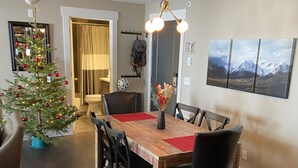 A dining area with a wooden table, black chairs, a Christmas tree, and a mountain landscape painting on the wall. - 207 Timbers Condominium (Crested Butte)