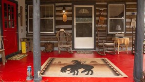 Une cabane rustique avec une porte rouge, une véranda en bois et une pancarte indiquant « Bienvenue ».