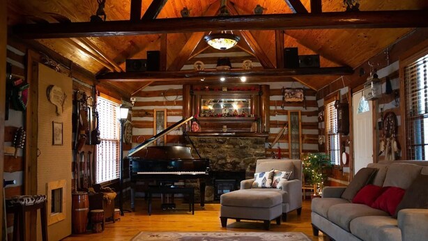 L’intérieur chaleureux d’un chalet en bois comprend un magnifique piano à queue, un fauteuil confortable et un canapé.