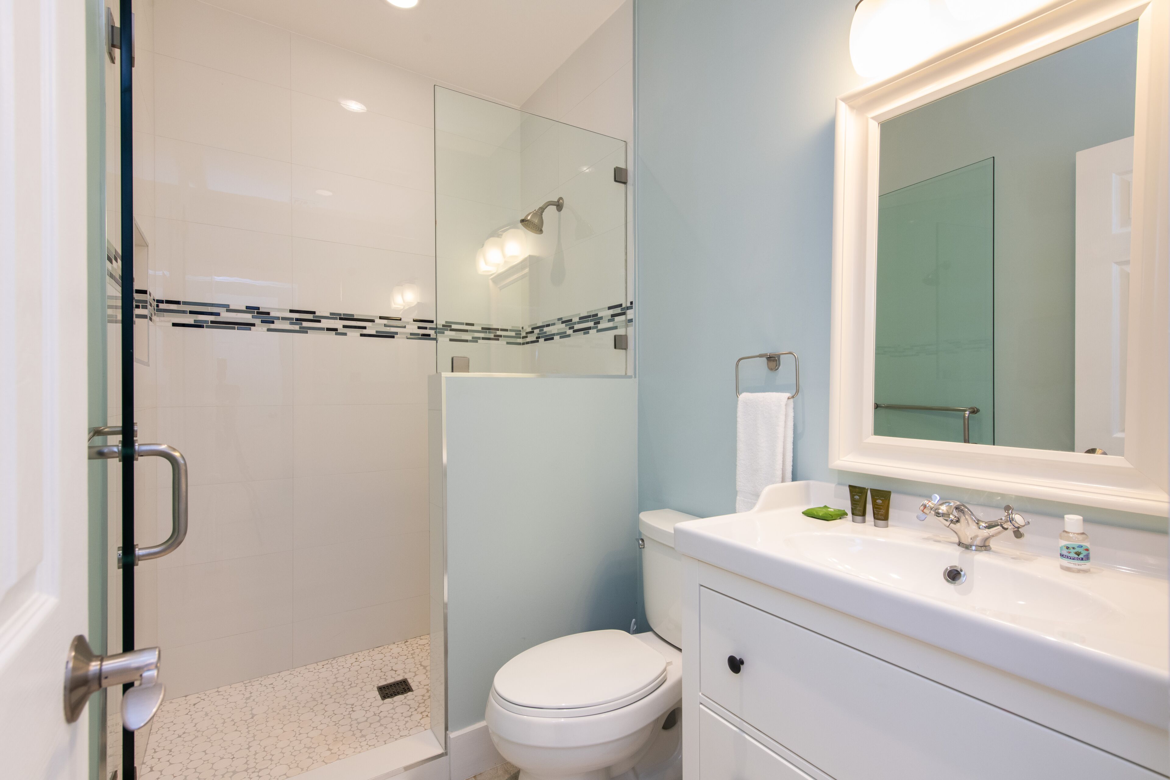 A modern bathroom with a glass shower enclosure, a white toilet, and a vanity with a mirror.