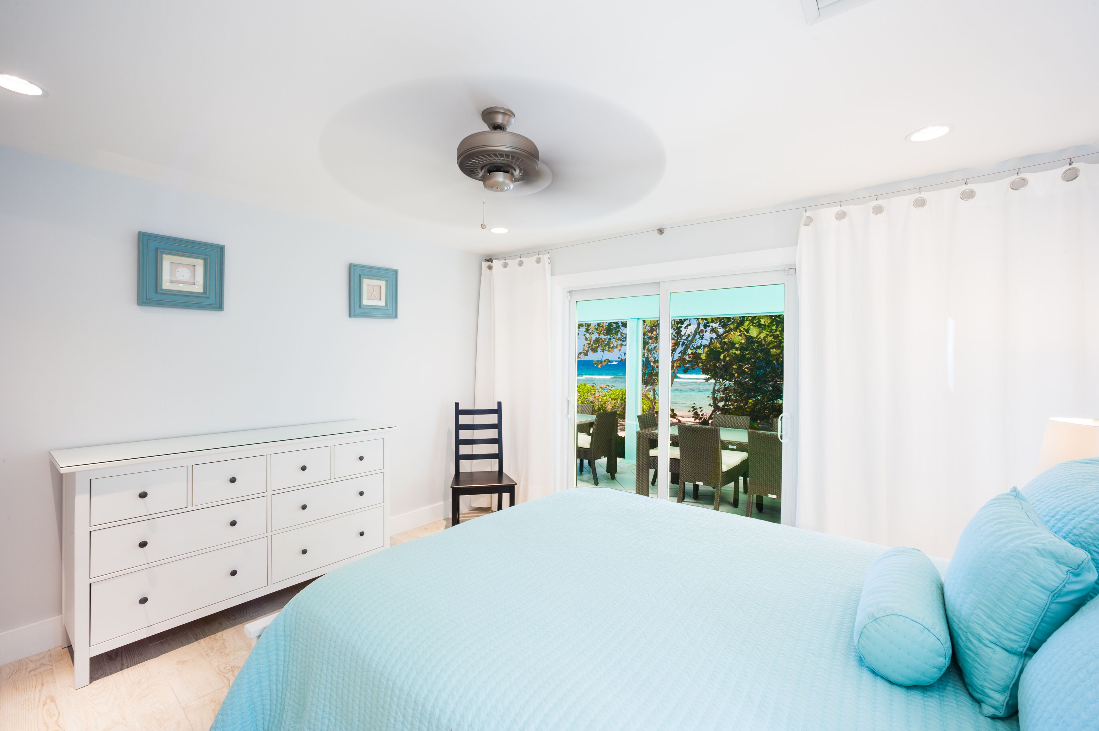 Un dormitorio con cama, cómoda, silla y vistas al exterior a través de un ventanal.