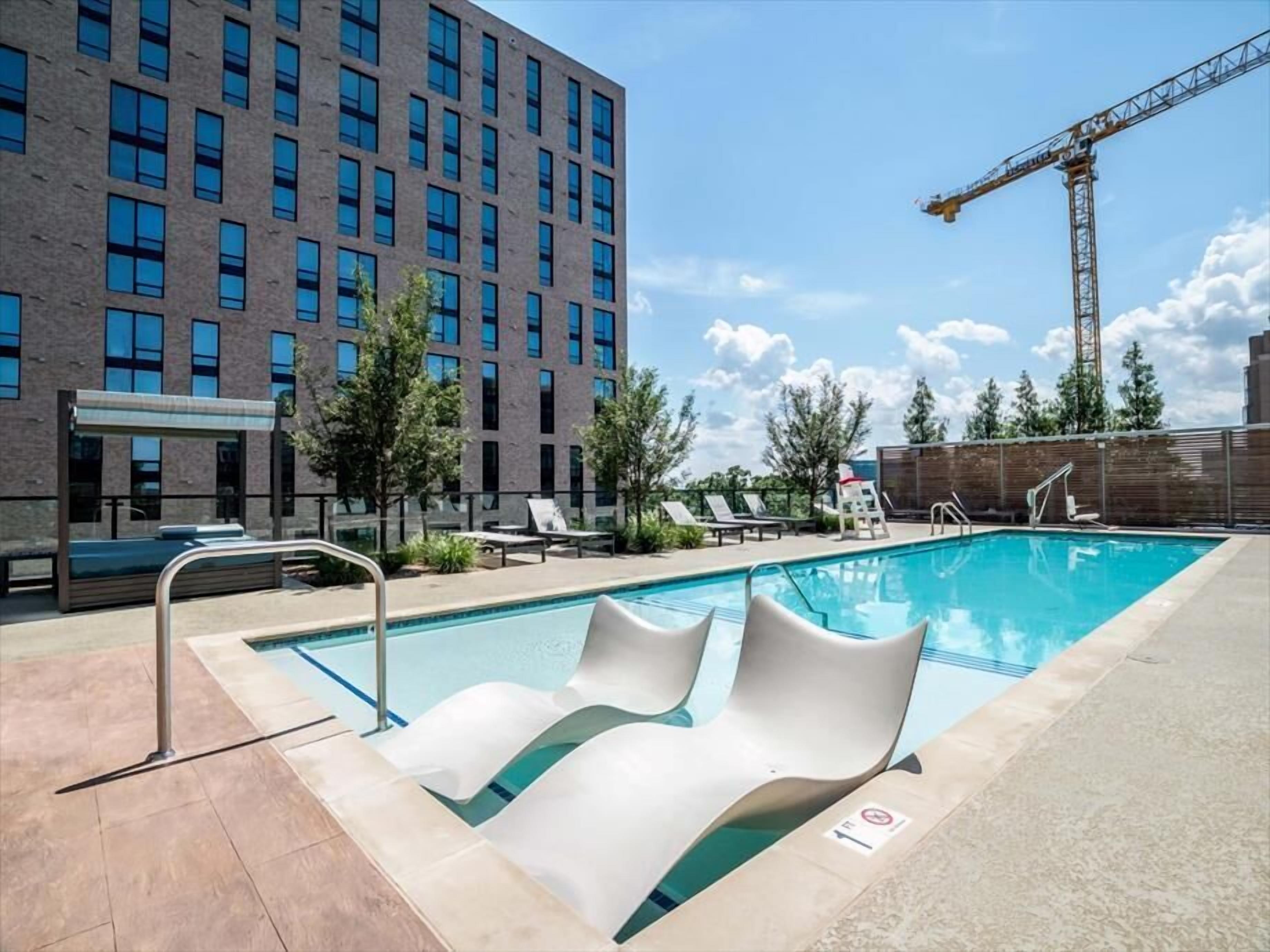 A modern outdoor pool area with lounge chairs and a view of a multi-story building.