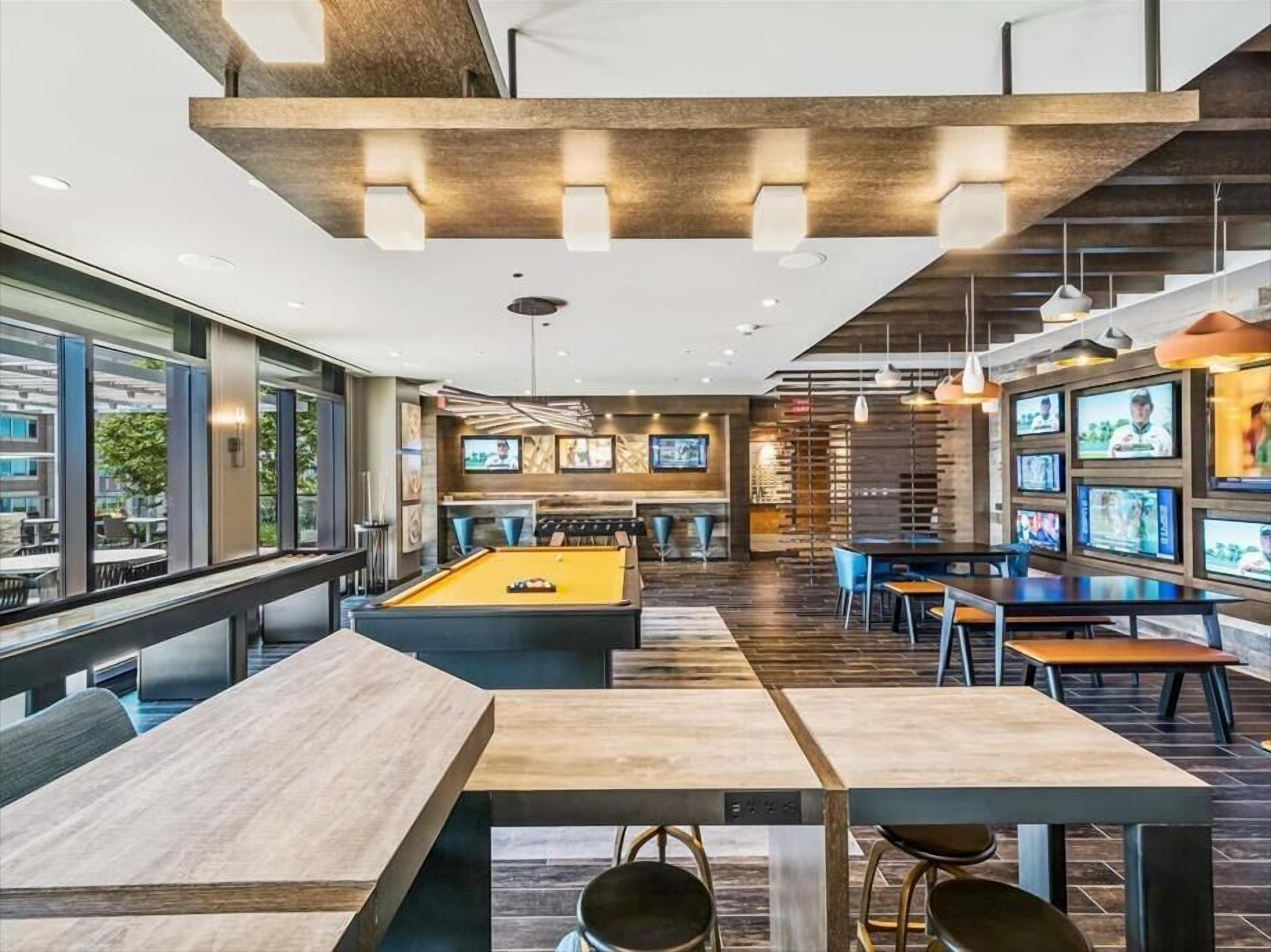 A modern indoor recreational area with a pool table, billiards, and multiple TV screens.