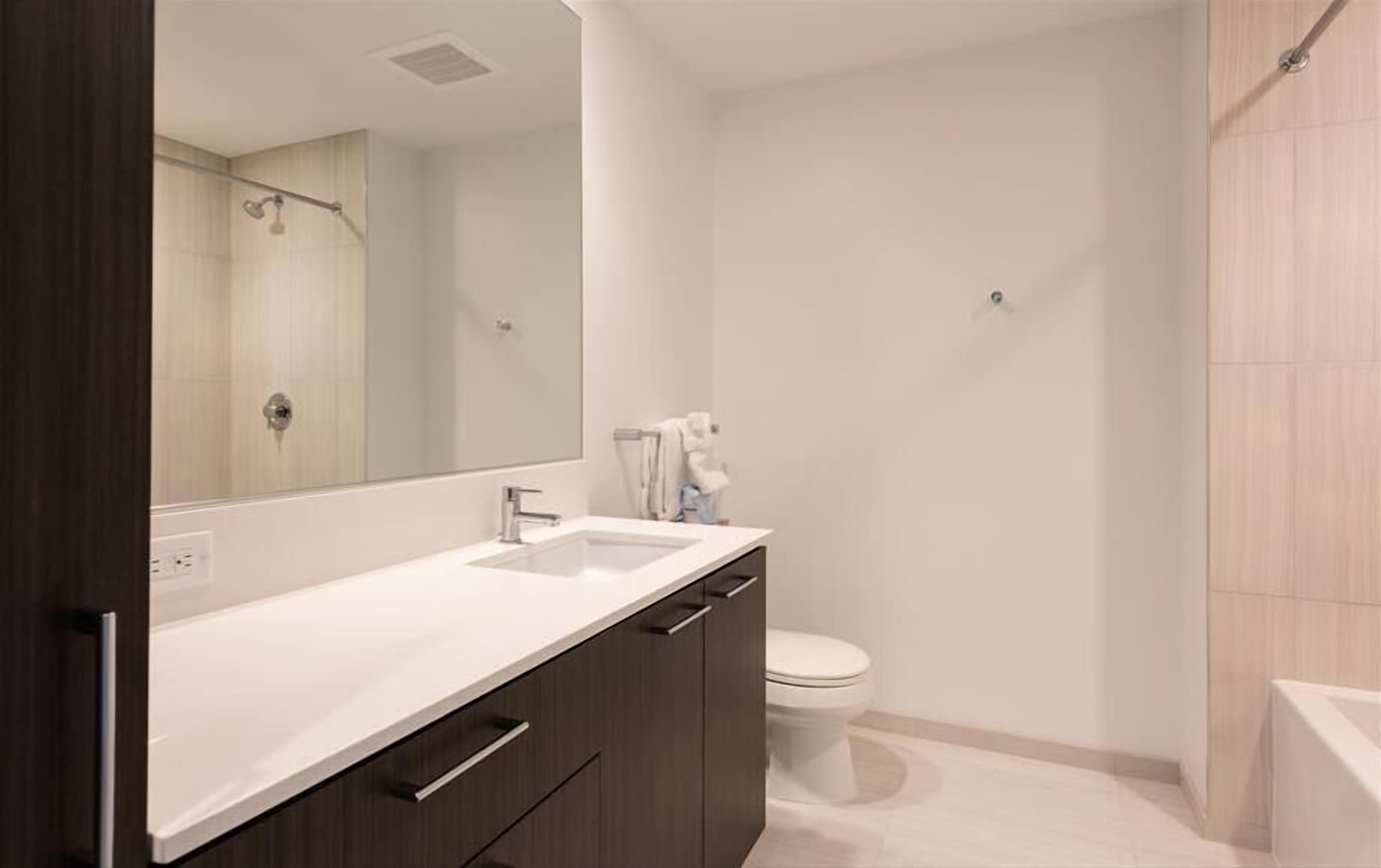 A modern bathroom with a large mirror, a sink, a toilet, and a shower area.