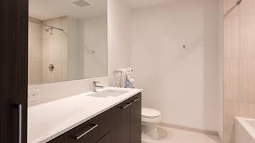 A modern bathroom with a large mirror, a sink, a toilet, and a shower area.
