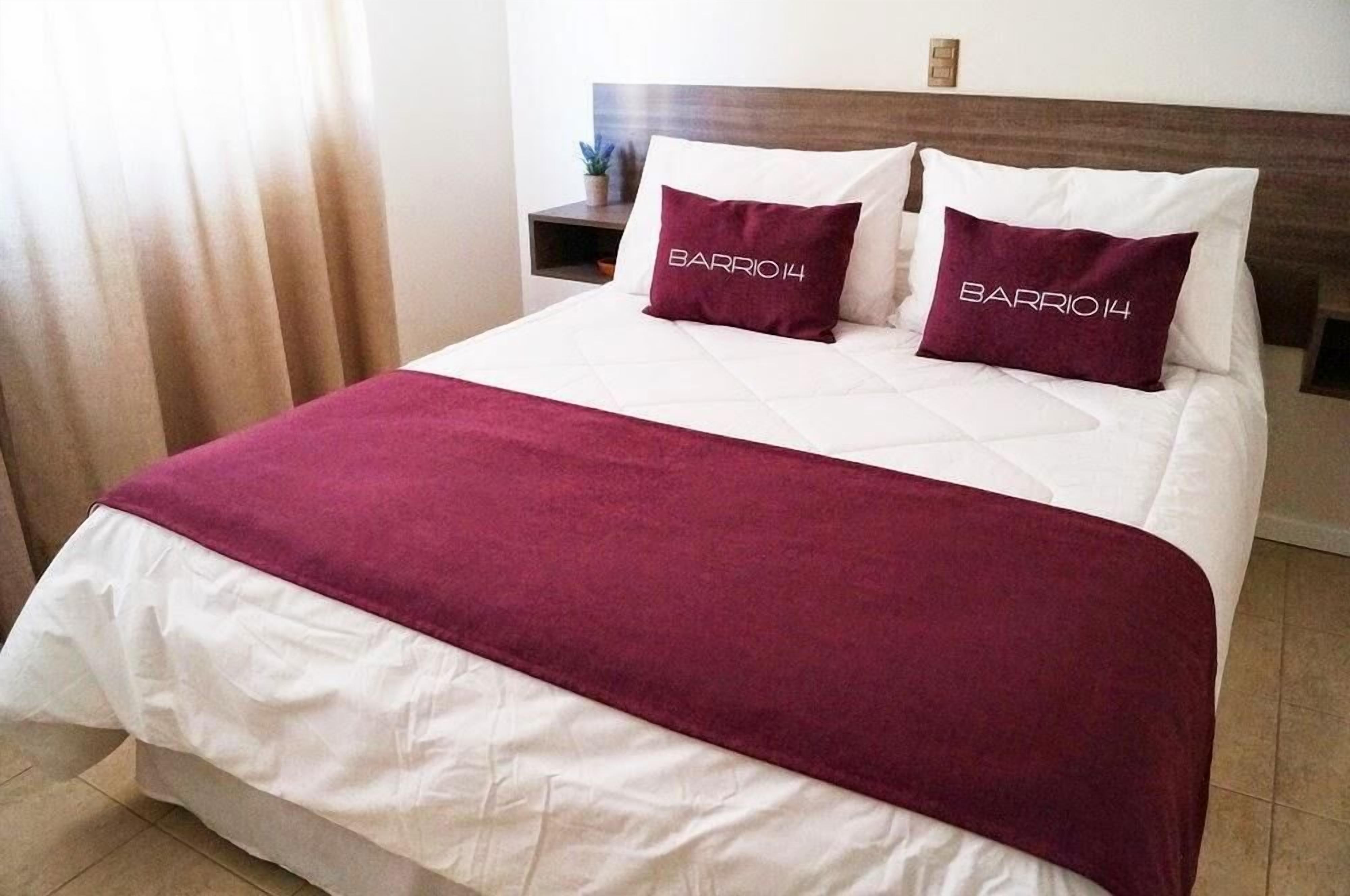 Una cama bien hecha con una colcha blanca y granate, dos almohadas a juego y un cabecero de madera.