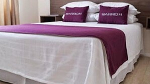 A neatly made bed with a white and purple bedspread, two pillows with the text "BAGHDAD," and a wooden headboard. - Hotel Barrio 14 (Antofagasta)