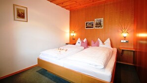 A double bed with white linens, two bedside tables with lamps, wooden paneling on the walls, and a framed picture on the left wall. - Apartment Westernberg 55sqm, terrace, kitchen, 1 bedroom, 1 bedsit. (Ruhpolding)