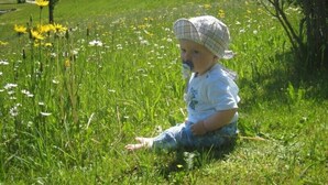 A child sitting in a grassy field with flowers and trees in the background. - Apartment Westernberg 55sqm, terrace, kitchen, 1 bedroom, 1 bedsit. (Ruhpolding)