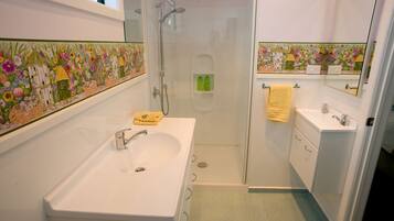 Un baño con un lavabo blanco, ducha con cerramiento de vidrio y un espejo sobre el lavabo.