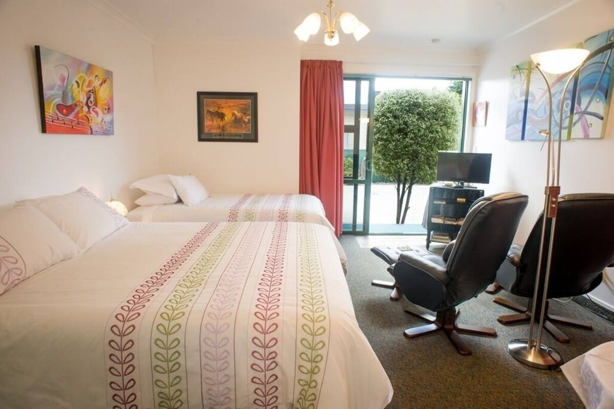 Habitación de hotel con dos camas, un escritorio, una silla, un televisor y obras de arte en las paredes.