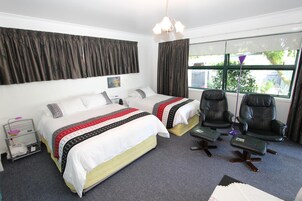 Habitación de hotel con dos camas, un escritorio, dos sillas, un ventanal con cortinas y una lámpara colgante.