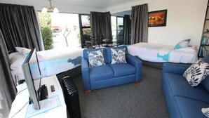 A hotel room with a bed, a blue sofa, a desk with a computer, and a bookshelf. - eMotel Napier (Napier)