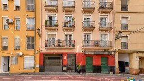 Un edificio de varios pisos con balcones, unidades de aire acondicionado y una entrada protegida por un portón.