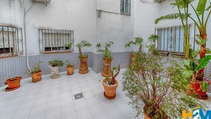 Un patio con plantas en macetas, suelo de baldosas y unidades de aire acondicionado en las paredes.