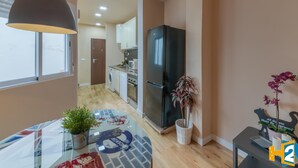Cocina moderna con un refrigerador negro, lavadora y microondas. Cuenta con un comedor con mesa de vidrio y plantas en macetas.