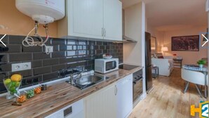 Una cocina moderna con microondas, estufa y lavabo. Hay un frutero en la encimera y un armario blanco arriba.