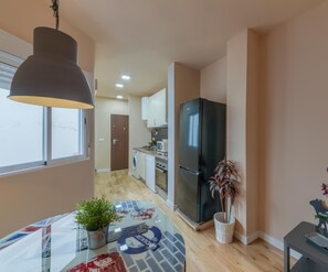 A modern kitchen with a black refrigerator, washing machine, and microwave. There is a dining area with a glass table and potted plants.