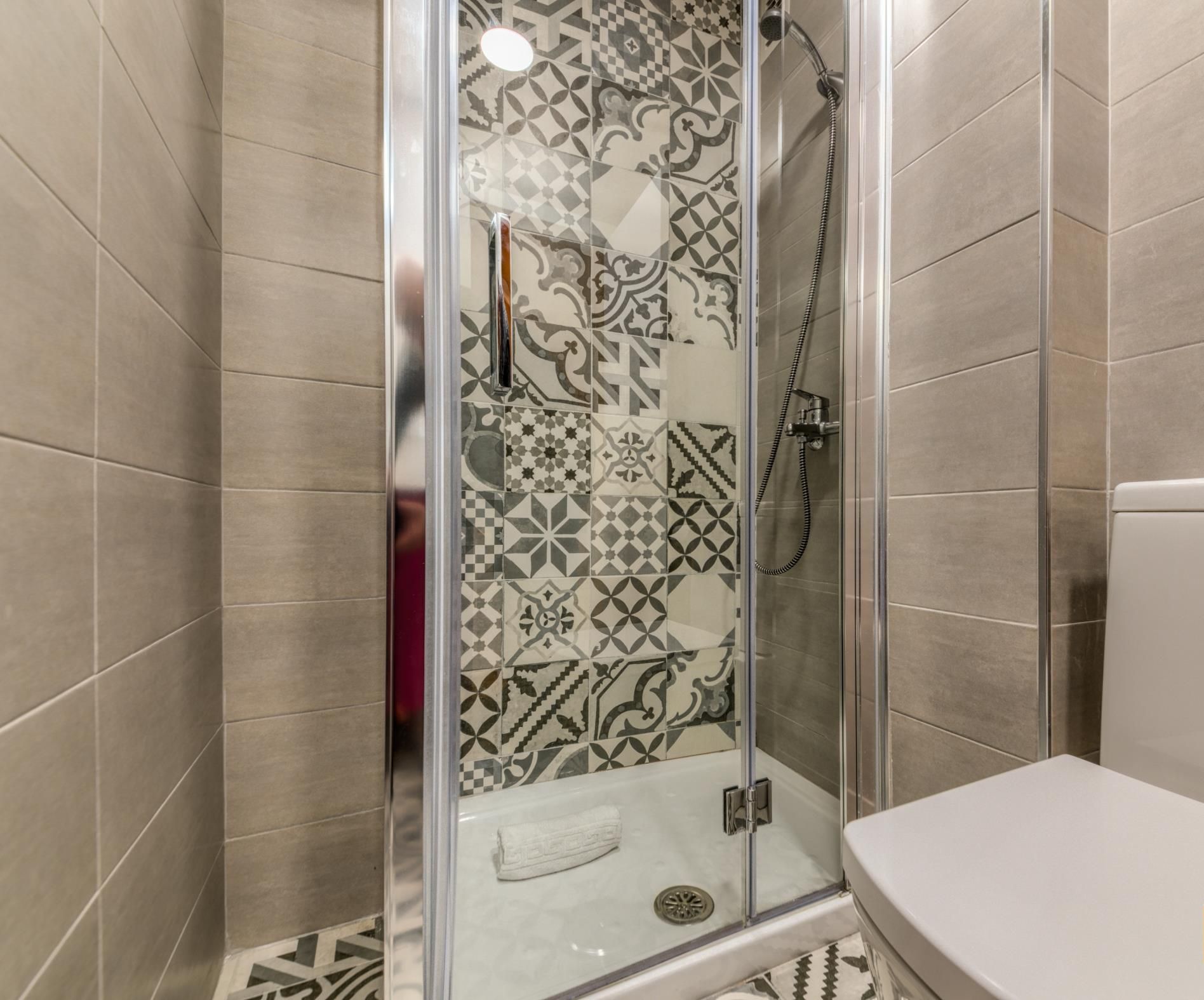 Doccia con porta in vetro, water e piastrelle decorate alle pareti.