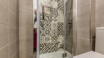 Doccia con porta in vetro, water e piastrelle decorate alle pareti.