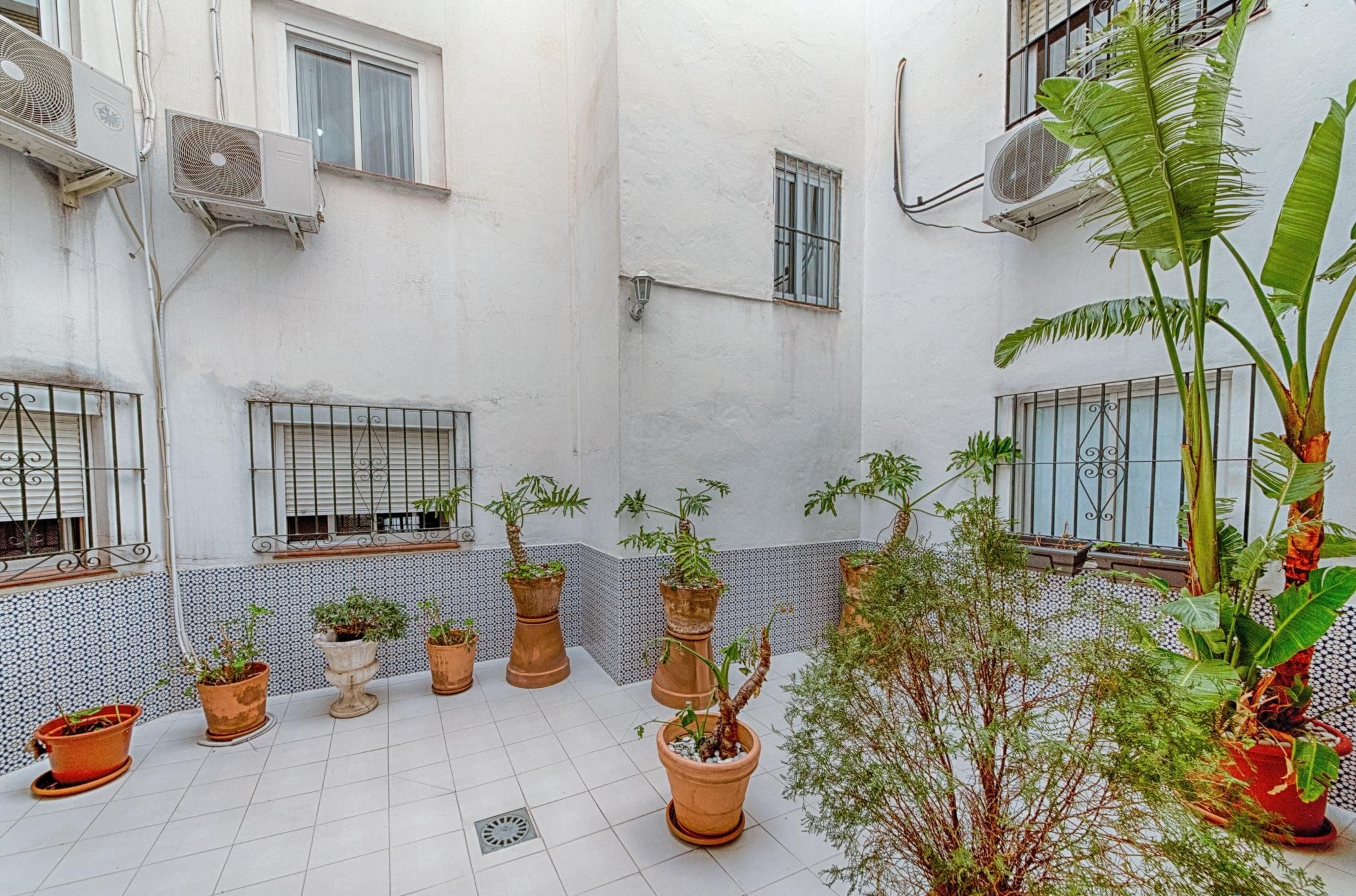 Un cortile con piante in vaso, pavimento piastrellato e condizionatori d'aria a parete.