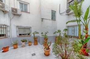 A courtyard with potted plants, tiled flooring, and air conditioning units on the walls.
