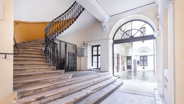 Un escalier orné de rampes en métal travaillées, menant à une porte.