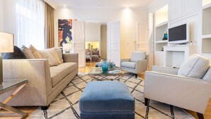 Un salon moderne avec un canapé, des fauteuils, une table basse en verre et un téléviseur fixé à un mur blanc.