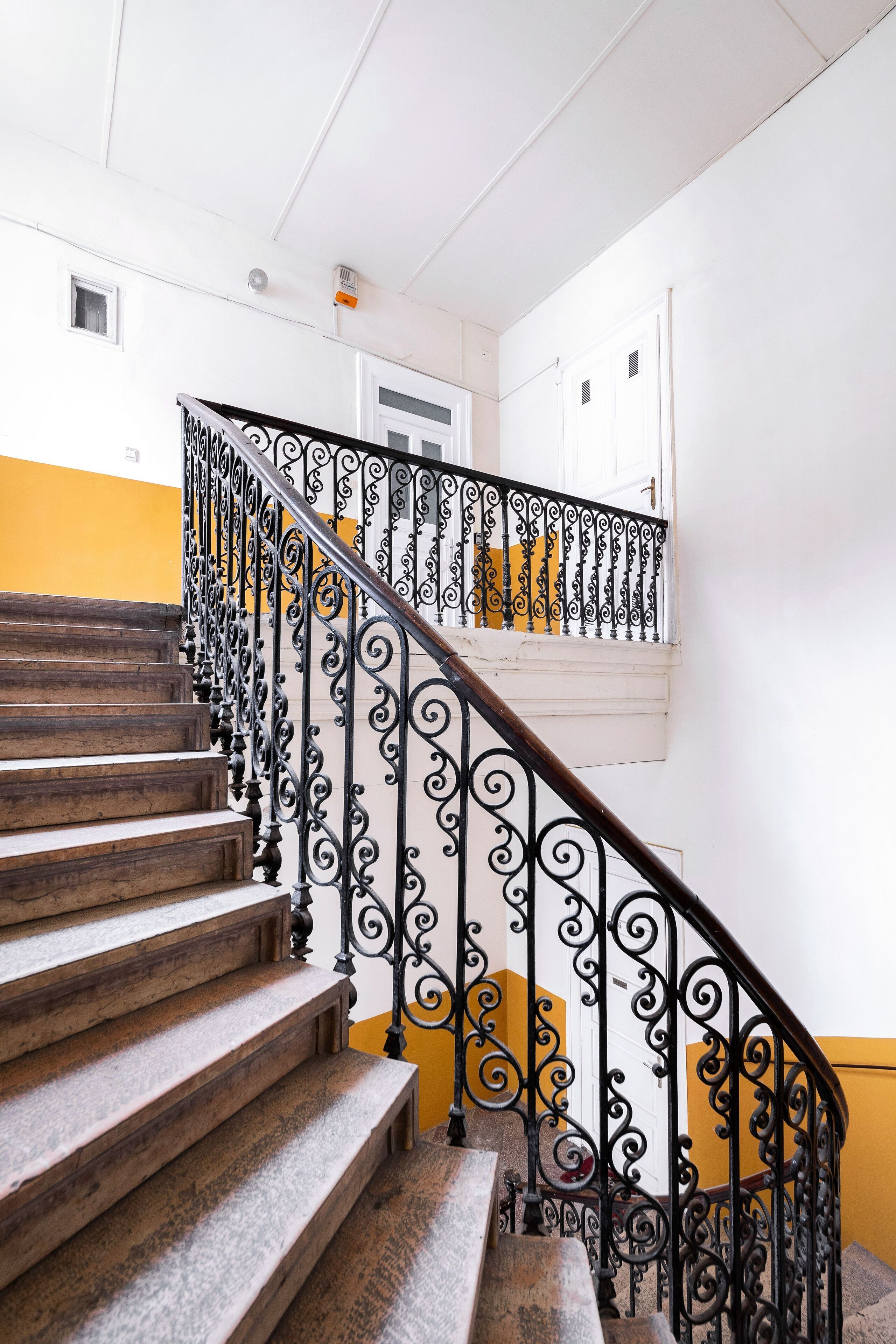 Un escalier avec des rampes en fer forgé noir décorées et des marches en bois.