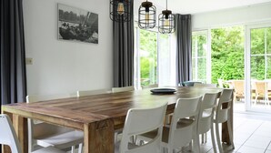 Un comedor con una mesa de madera, sillas blancas y lámparas colgantes.