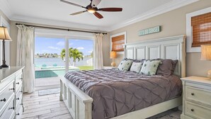 Une chambre avec un lit, un ventilateur de plafond, une table de chevet et une vue sur une piscine et des palmiers.