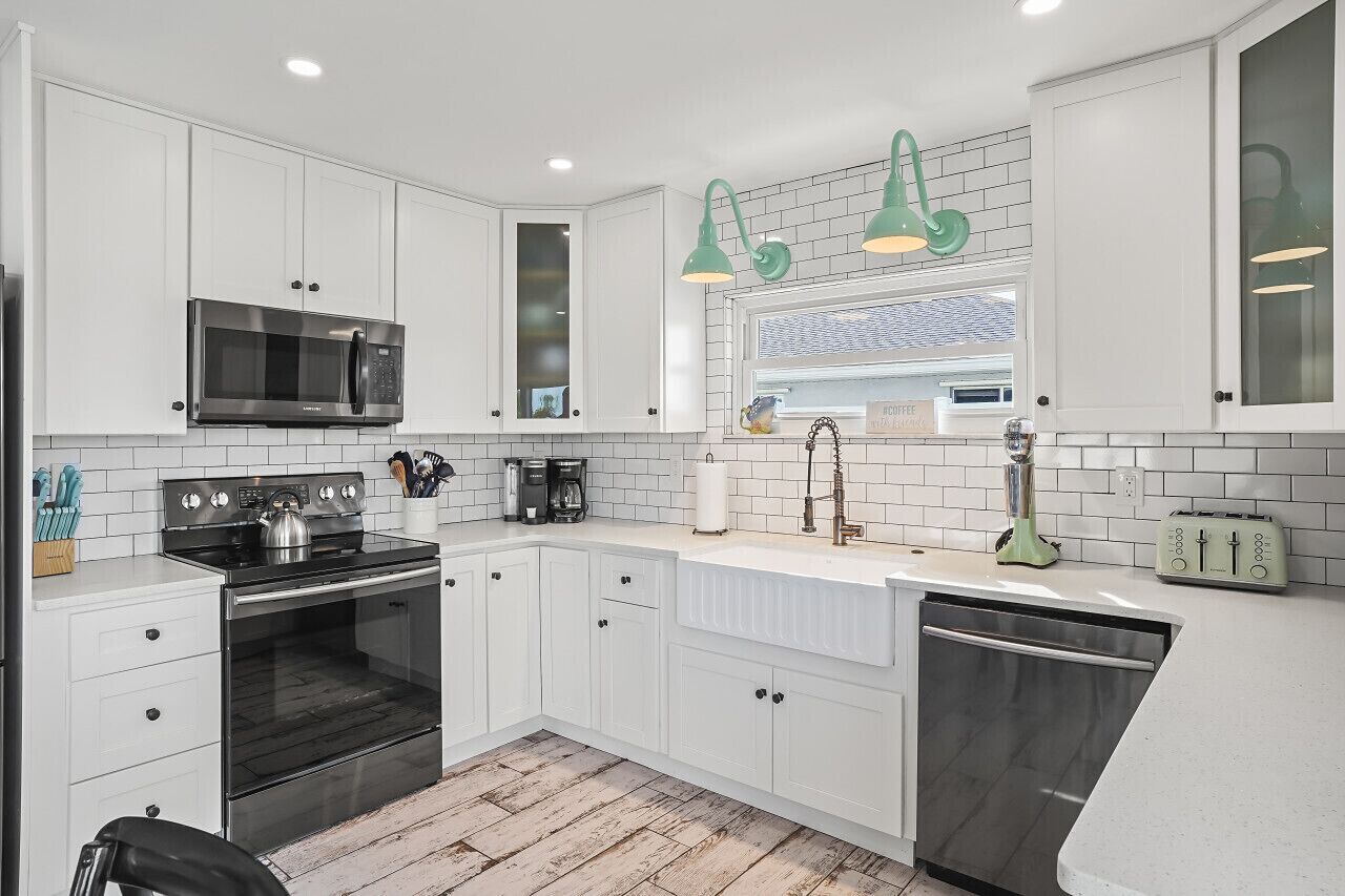 A modern kitchen with white cabinets, a stainless steel microwave, a kettle, a coffee maker, and a dishwasher.