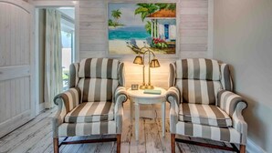 Une pièce avec deux fauteuils à rayures, une petite table avec des lampes et un tableau représentant une scène de plage accroché au mur.