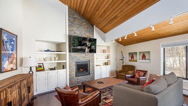 A cozy living room with a fireplace, wooden ceiling, and a large window. - SPECTACULAR BALDY VIEW REMODELED 2 BD TOWNHOME NEXT TO LIFTS! LUXURY! LOCATION! (Ketchum)