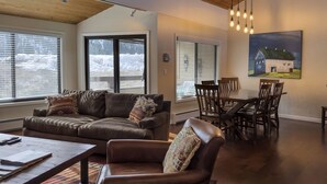 A cozy living room with a brown leather sofa, a wooden coffee table, and a dining area with wooden chairs and a table. - SPECTACULAR BALDY VIEW REMODELED 2 BD TOWNHOME NEXT TO LIFTS! LUXURY! LOCATION! (Ketchum)