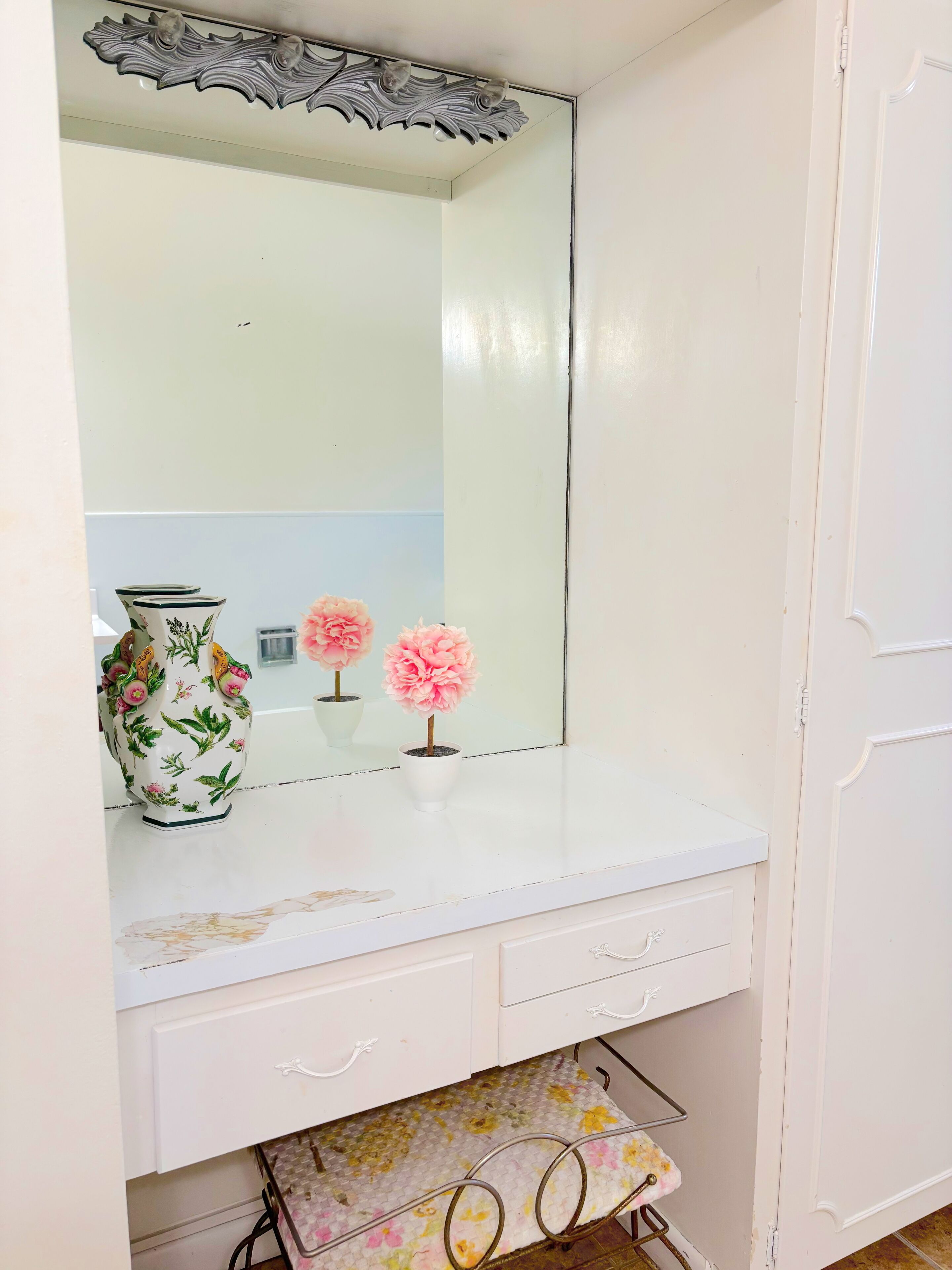 A bathroom vanity with a large mirror, a decorative vase, and a potted plant.