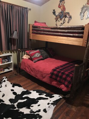 A bunk bed with a red blanket and pillows, a wooden bookshelf, a cowhide rug, and a wall mural of a horse and rider. - Madison Valley Cabin (Cameron)