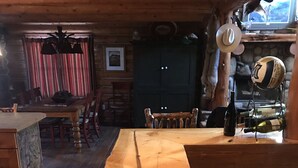 Uma área de bar com balcão de madeira, um longo banco, teto rústico e uma lareira de pedra ao fundo.