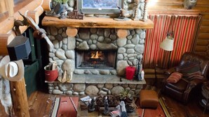 Interior acolhedor de uma cabana com lareira de pedra, móveis de madeira e decoração rústica.