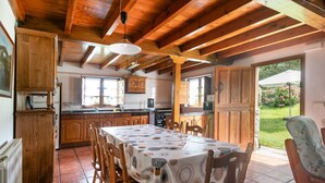 A wooden interior with a dining table set for four, kitchen cabinets, and a view of a garden through a door. - House with Garden and Barbecue in Llanes - Molinin (Ardisana)