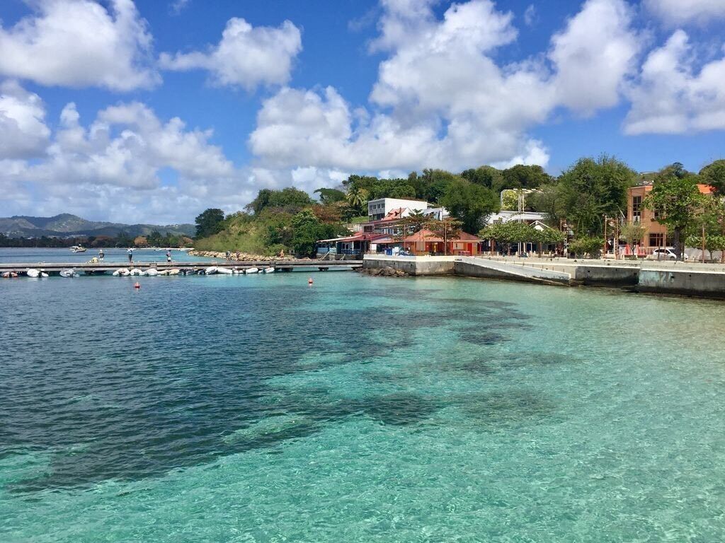 A coastal area with clear turquoise water, a pier, and buildings with balconies overlooking the sea.