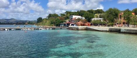 A coastal area with clear turquoise water, a pier, and buildings with balconies overlooking the sea.